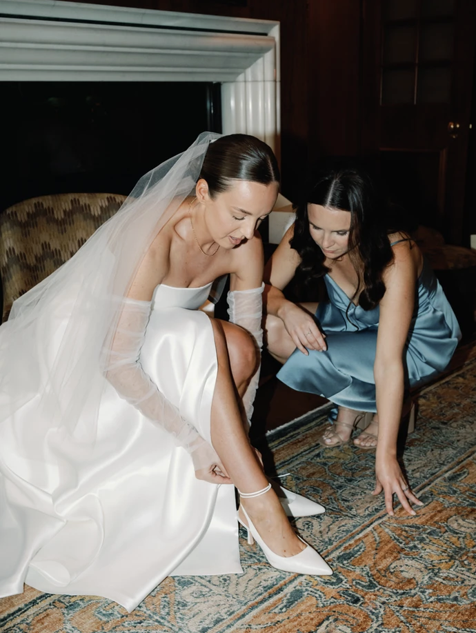 documentary photo of Bridal and bridesmaid dressing and getting ready on wedding day as they fix shoe Photo by Jessica Lily